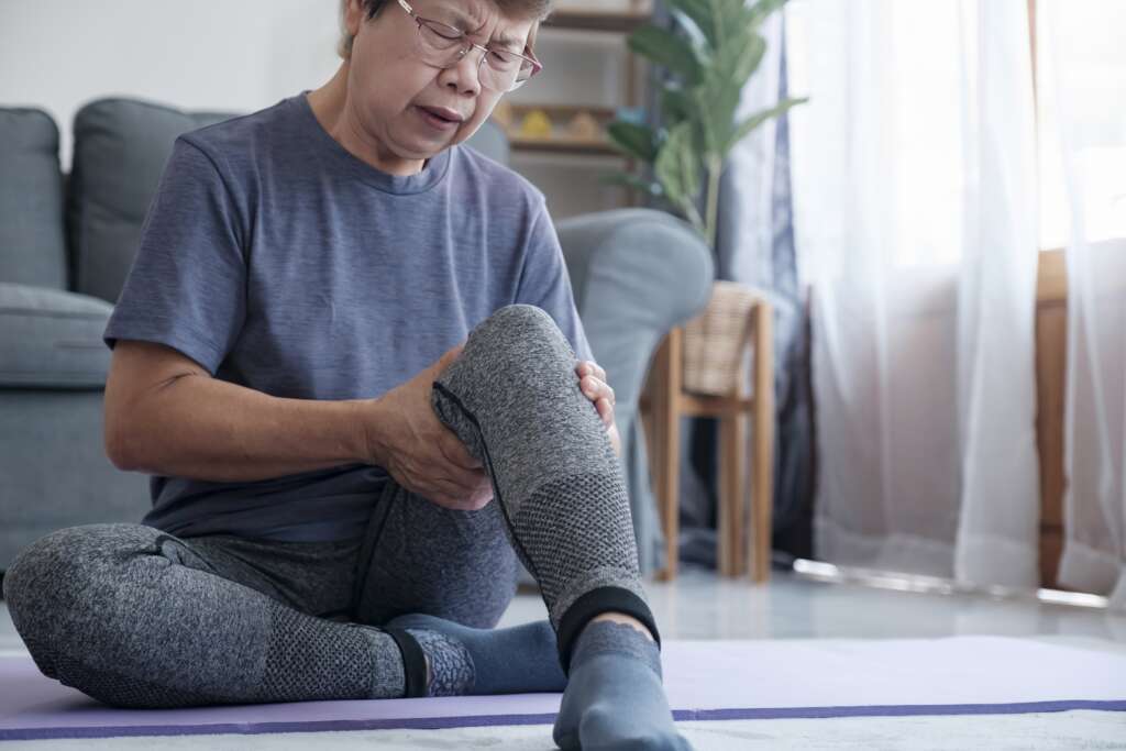 A middle aged woman holds her knee and thigh and her face expresses discomfort. The image is relating to an article about physiotherapy and how it can treat knee issues.