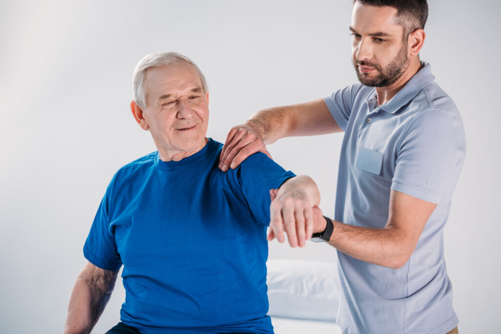 portrait of physiotherapist doing massage to smiling senior man on massage table receiving physiotherapy for a rotator cuff injury