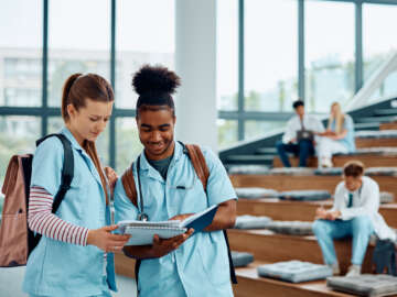 physiotherapy students in a lecture hall discussing a concept. There are other students in the background. This is part of an article written by a student about physiotherapy online services and where online versus face to face physio is appropriate.