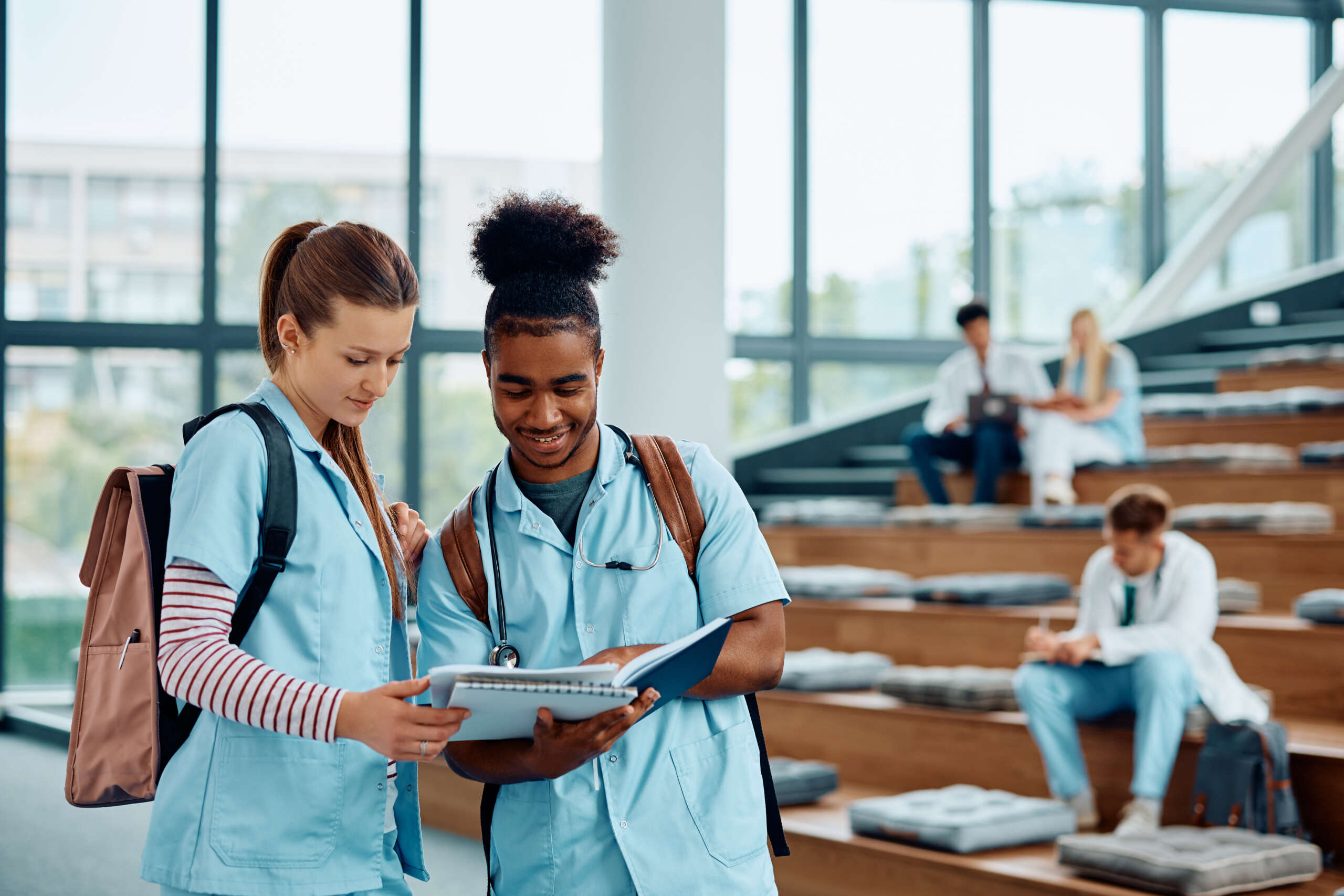 physiotherapy students in a lecture hall discussing a concept. There are other students in the background. This is part of an article written by a student about physiotherapy online services and where online versus face to face physio is appropriate.