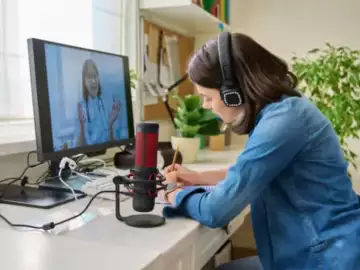 Woman sat at a desk with a microphone and headphones on, talking via a screen to a healthcare professional