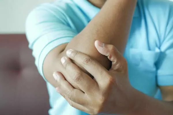 Close up of someone holding their elbow wearing a blue tshirt. Implication of tennis elbow,