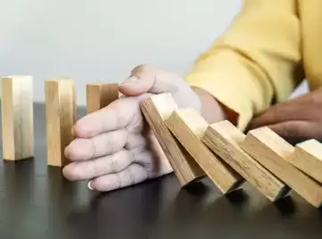 hand stopping falling collapse wooden block dominoes effect from continuous toppled block, falls prevention and development of balance and stability.