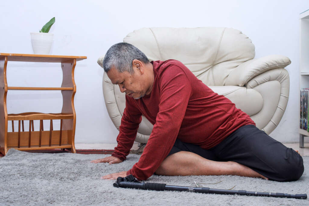 Elderly / older man who has fallen on the floor alone with walking stick preventing falls