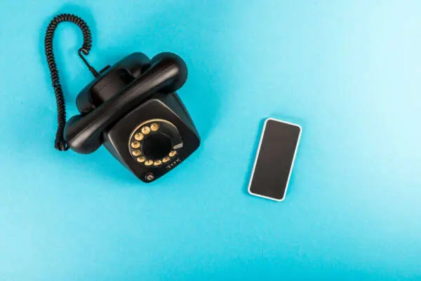 A 1960s telephone next to a modern smartphone on a blue background