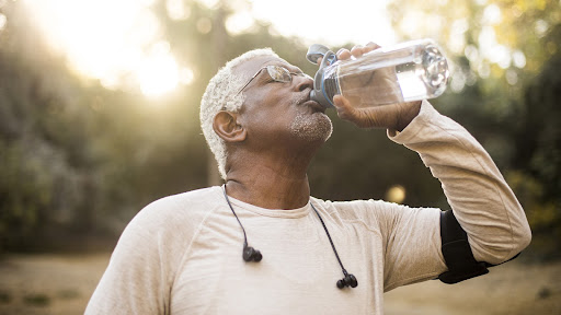 older man drinking water outdoors after exercising. Black man middle aged. Brighton and Hove physiotherapy